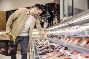 Zdjęcie - wesoly-mezczyzna-wybiera-mieso-w-supermarkecie-trzymajac-wozek-na-zakupy