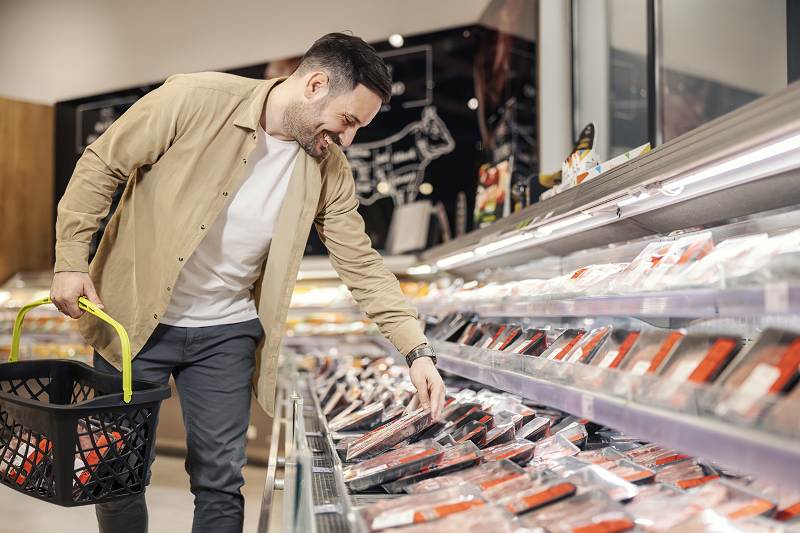 Zdjęcie - wesoly-mezczyzna-wybiera-mieso-w-supermarkecie-trzymajac-wozek-na-zakupy